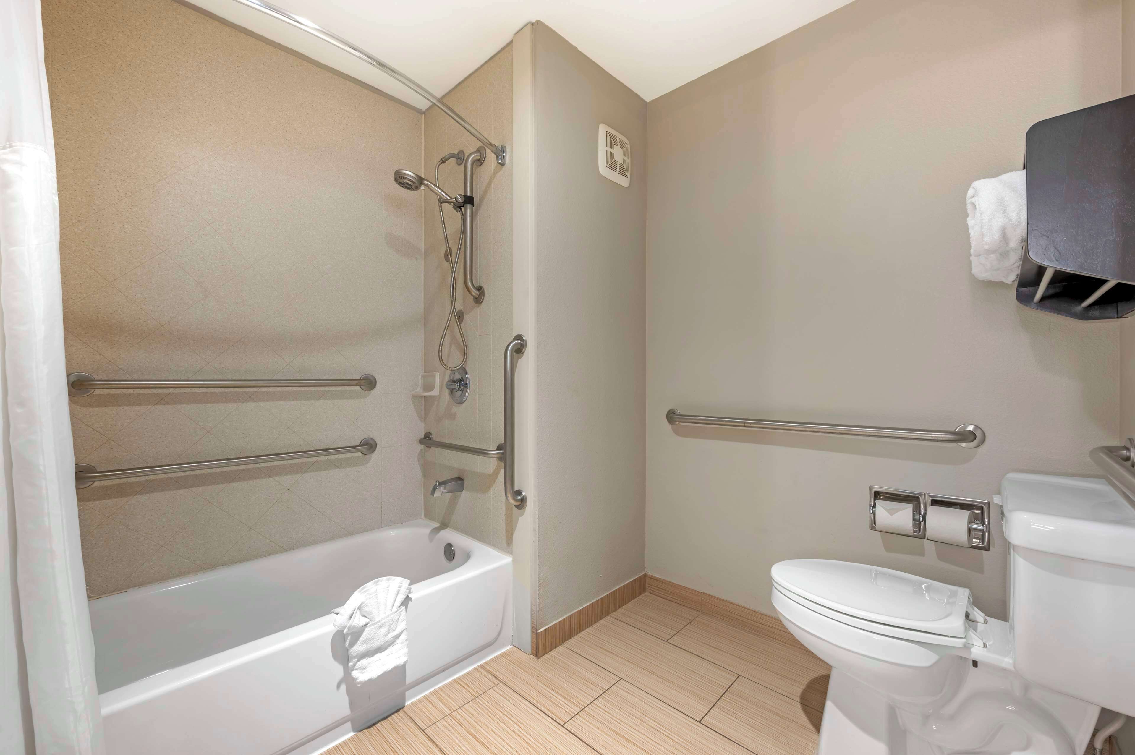 A bathroom with a bathtub, toilet, and shower. It includes grab bars and a towel rack.