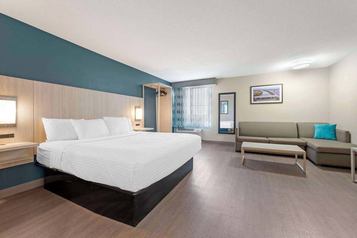 A modern hotel room with a large bed, a sofa, a desk, and a window with curtains.