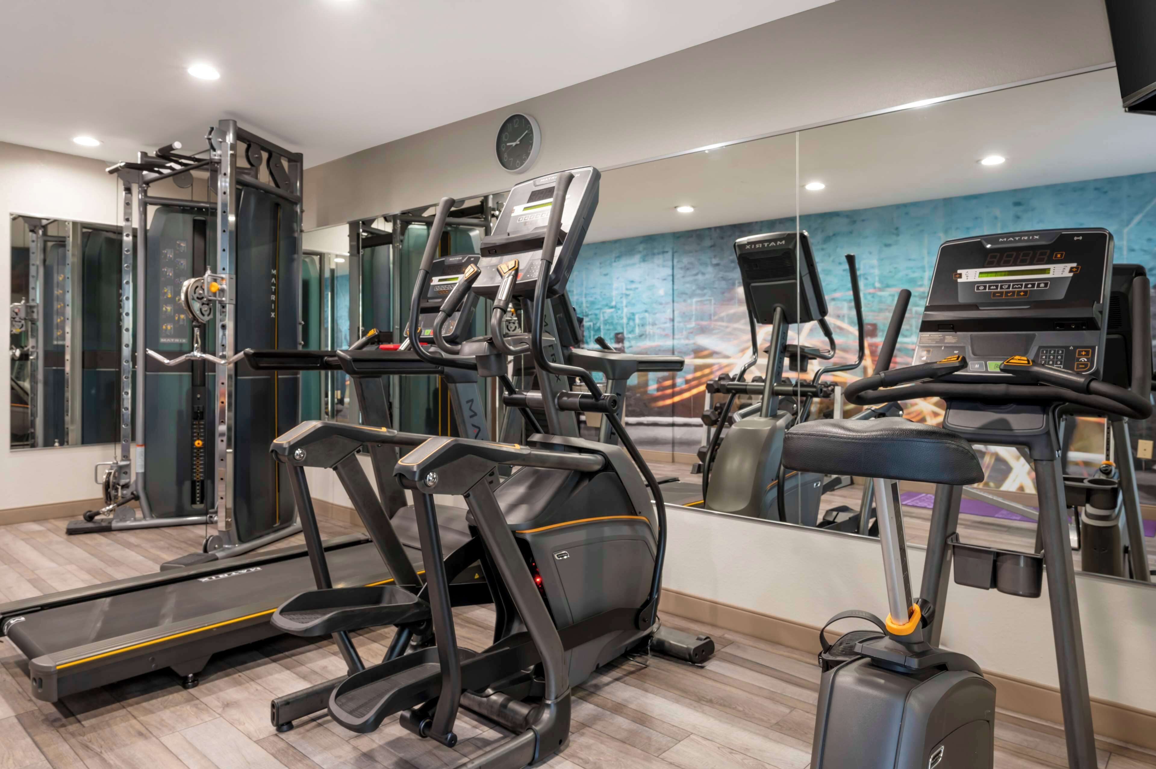 A modern gym with various exercise equipment including treadmills, a weight machine, and a mirror wall.