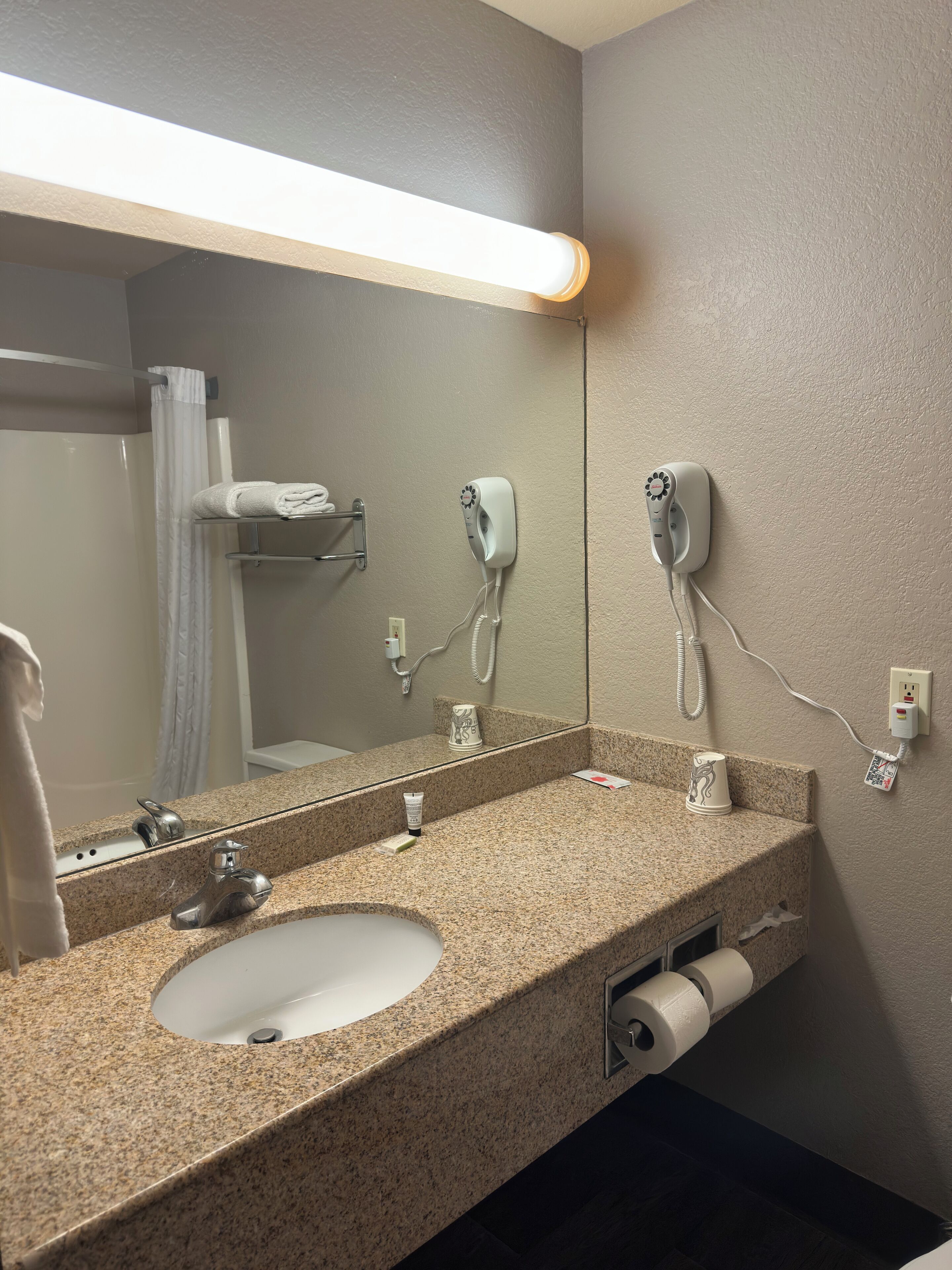 A bathroom with a granite countertop, a sink, a mirror, a hairdryer, and a towel rack.
