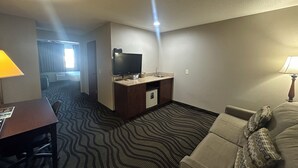 Een hotelkamer met een kitchenette, een televisie, een bank en een kamerbreed tapijt met een patroon.
