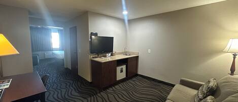 Habitación de hotel con kitchenette, televisión, sofá y alfombra estampada.