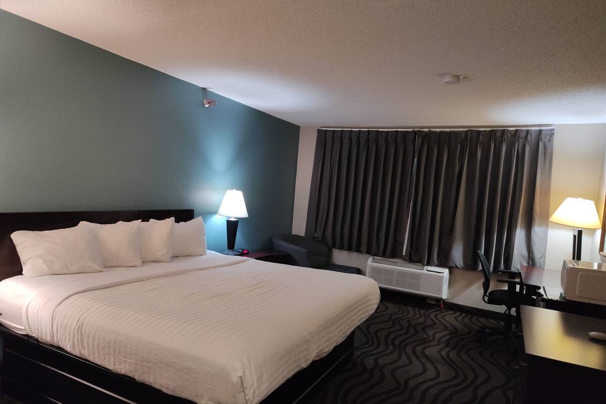 Une chambre d’hôtel avec un grand lit, deux lampes de chevet, une chaise, un bureau et une fenêtre avec des rideaux.