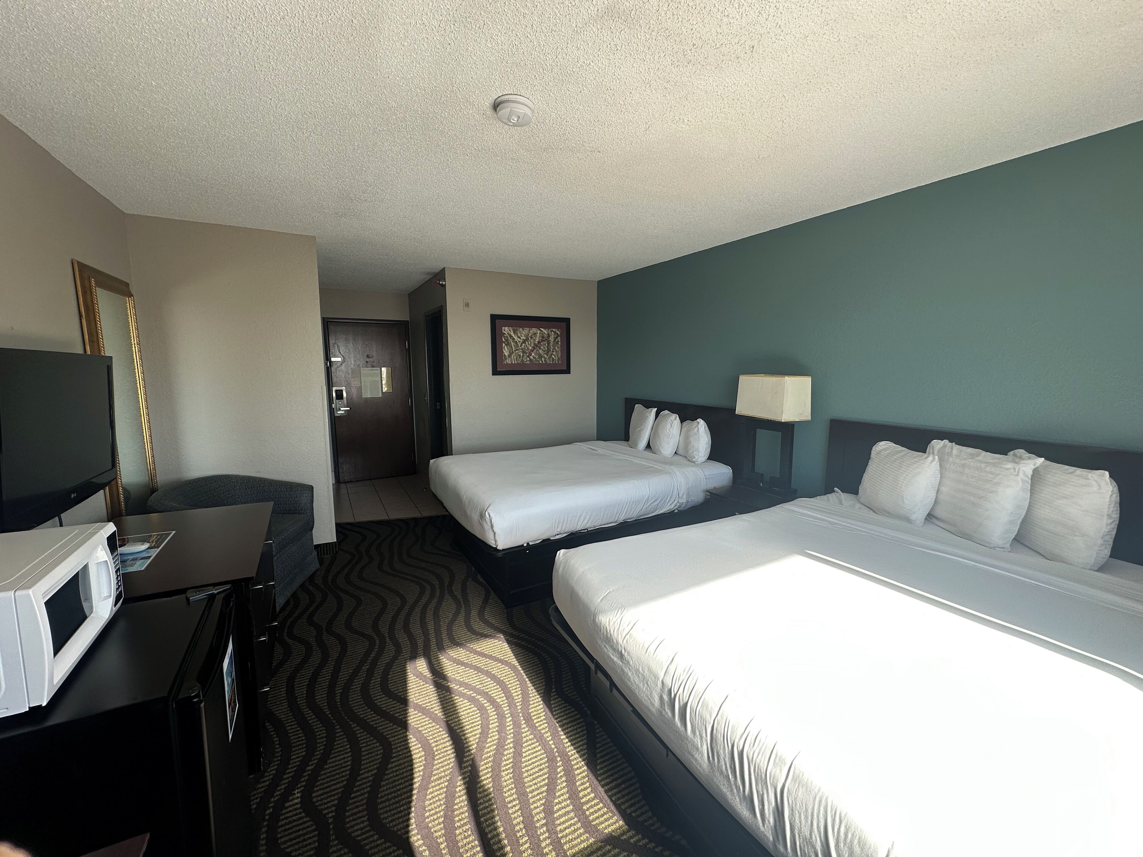 A hotel room with two beds, a desk with a television, a microwave, and a door leading to a bathroom.