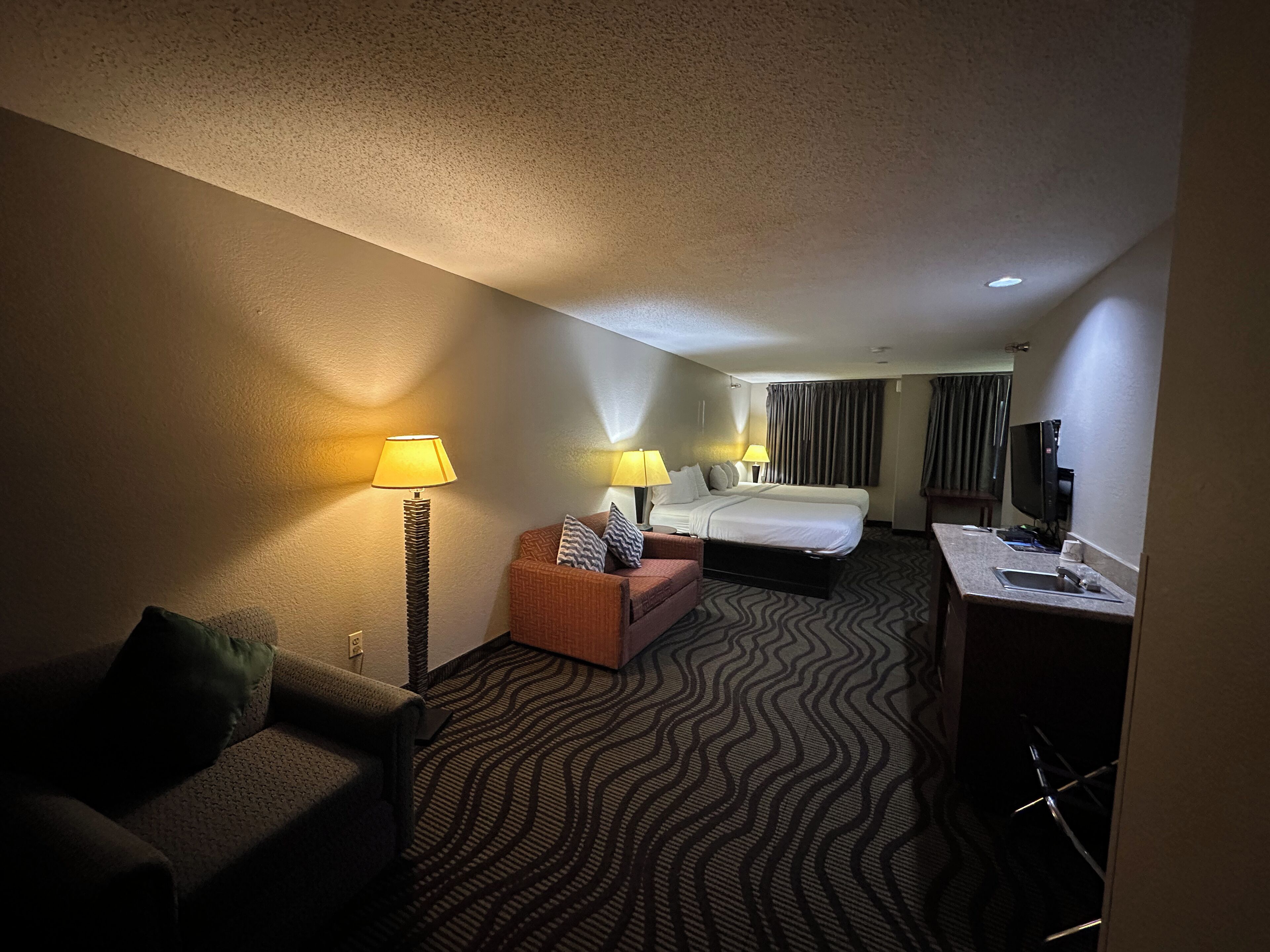 Ein Hotelzimmer mit Bett, Sofa, Schreibtisch und Computer sowie einem Fernseher.