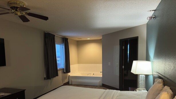 Hotelkamer met een groot bed, een plafondventilator, een raam met gordijnen, een badkuip en een bedlampje.