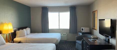 Habitación de hotel con dos camas, un escritorio, una silla, un televisor y una ventana con cortinas.
