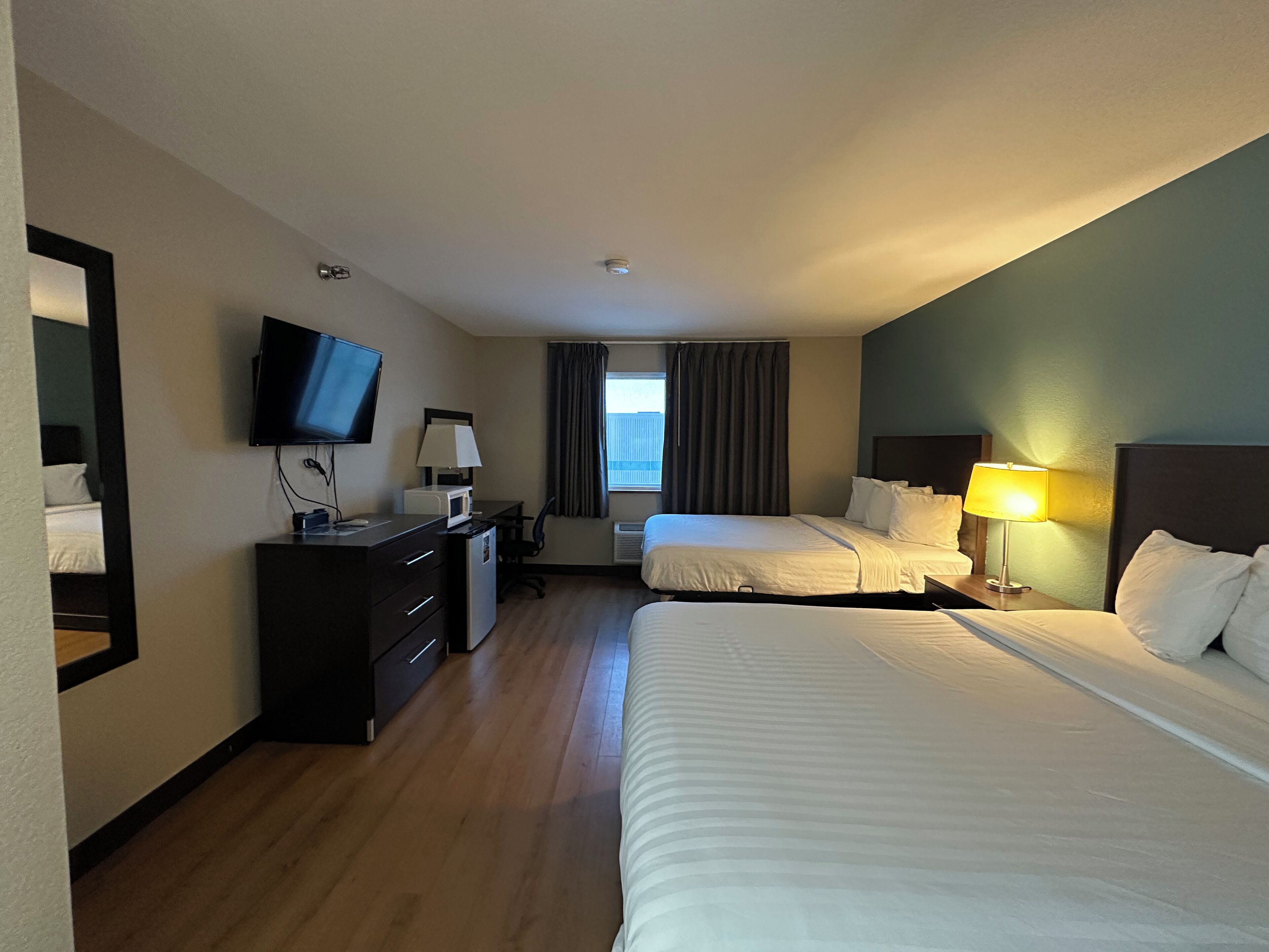 Habitación de hotel con dos camas, un escritorio con ordenador, televisión y ventana con cortinas.