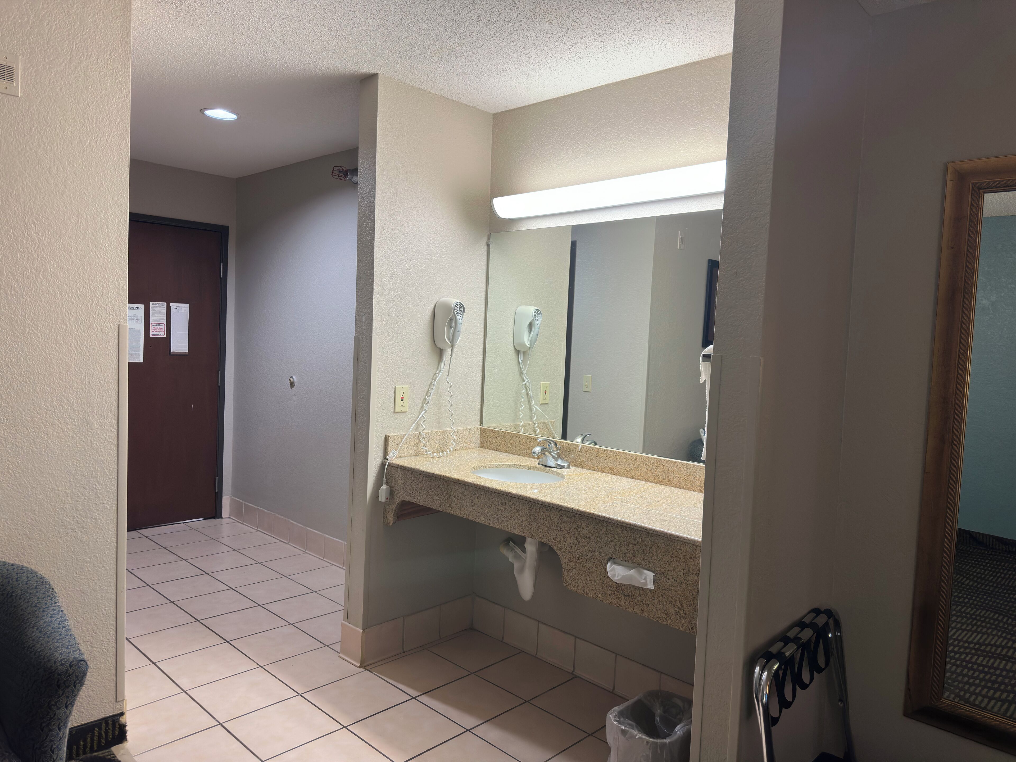 A hotel bathroom with a sink, mirror, hairdryer, and a trash bin.