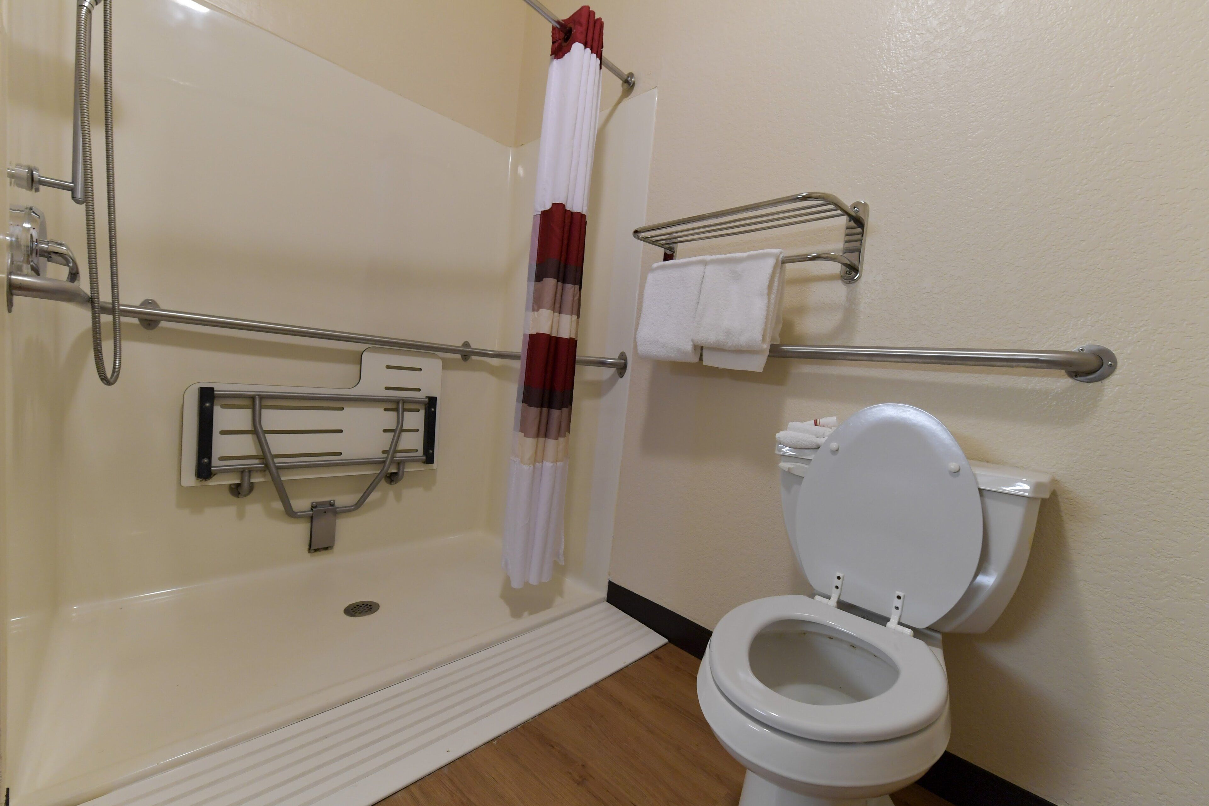 A bathroom with a shower, grab bars, a toilet, and a towel rack.