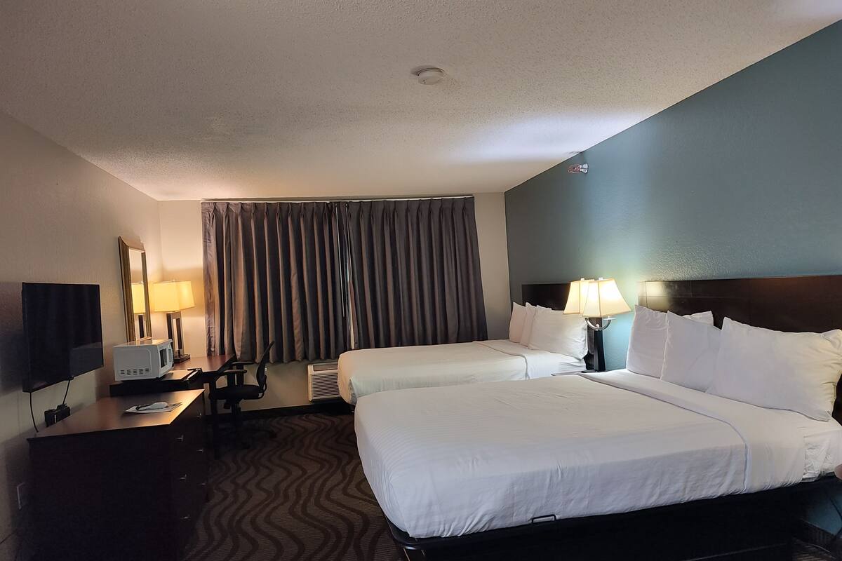Une chambre d’hôtel avec deux lits, un bureau doté d’une télévision à écran plat, un four à micro-ondes et une lampe.