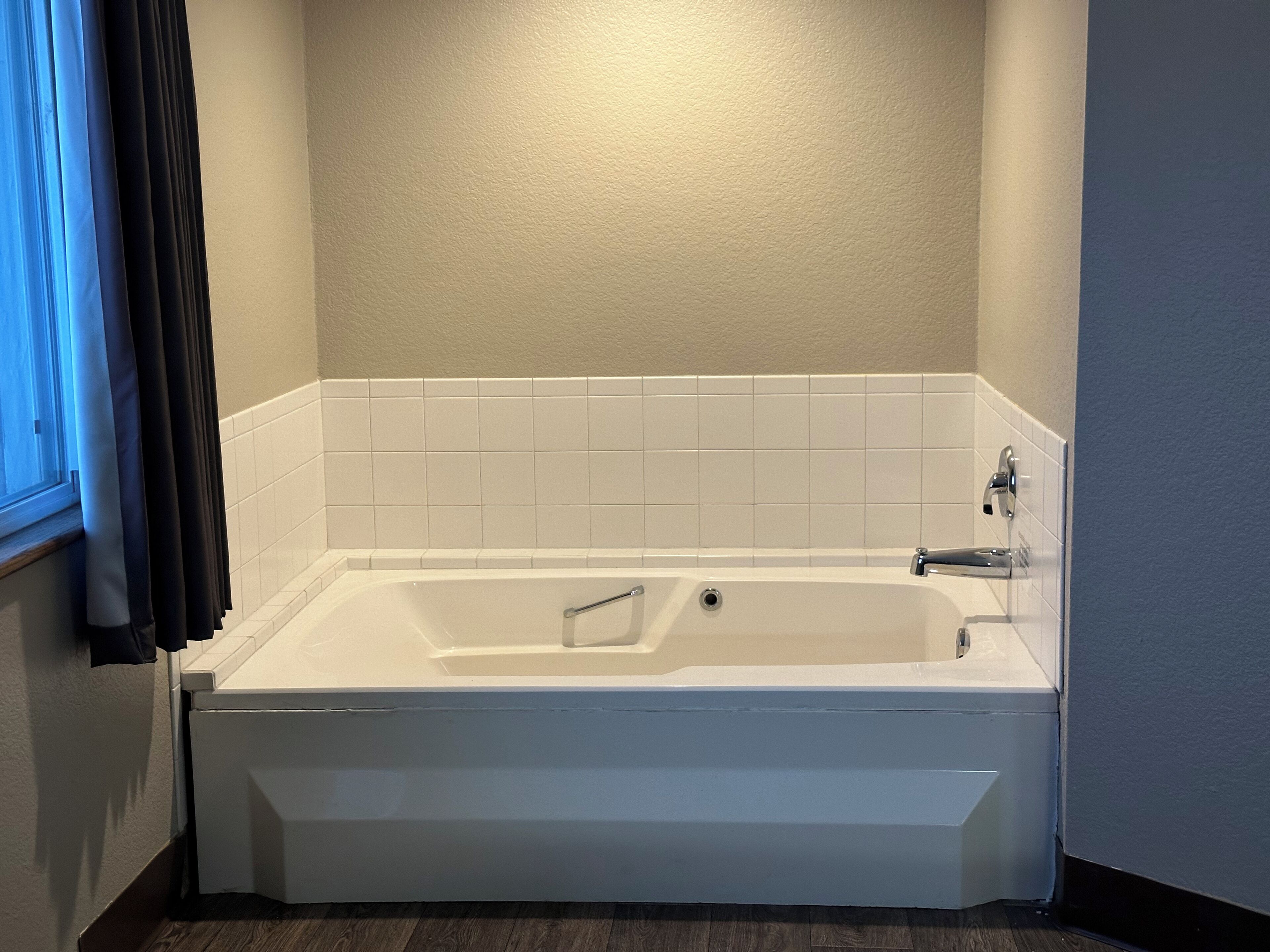 A standard white bathtub with a showerhead, tiled walls, and a window with curtains.