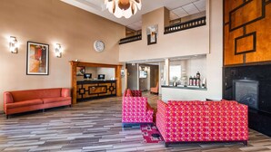 A hotel lobby with a reception desk, a red sofa, patterned couches, a wooden floor, and a fireplace.