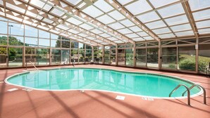 A covered indoor swimming pool with clear glass walls, a tiled floor, and a pool ladder.