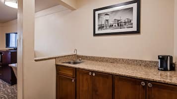 Una kitchenette con encimera de granito, un lavamanos, armarios de madera y un cuadro con una vista urbana enmarcada en la pared.