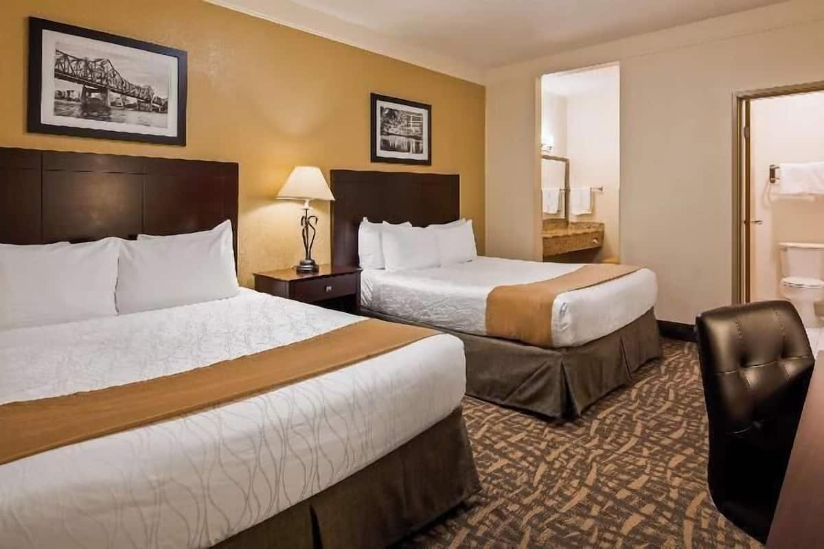 A hotel room with two beds, a desk, a chair, a TV, and a bathroom visible through an open door.