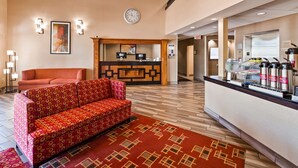 A hotel lobby with a reception desk, a sofa, a clock, and a coffee station.