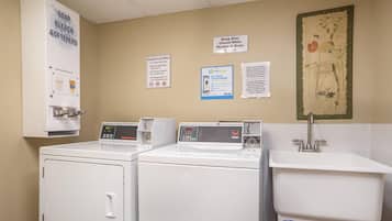 A laundry area with two washing machines, a sink, and various signs including one for guest laundry and another for payment.