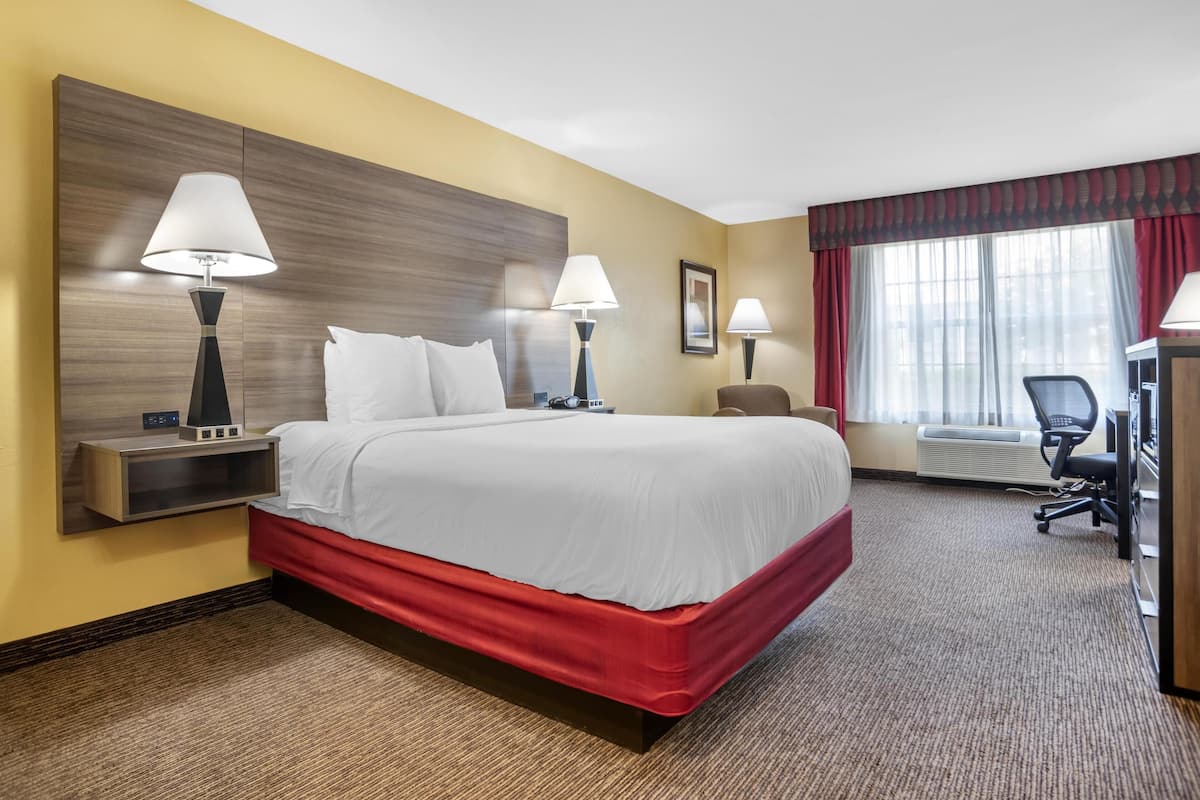 Habitación de hotel con una cama grande, dos lámparas de noche, un escritorio con silla, una ventana con cortinas y un aire acondicionado instalado en la pared.