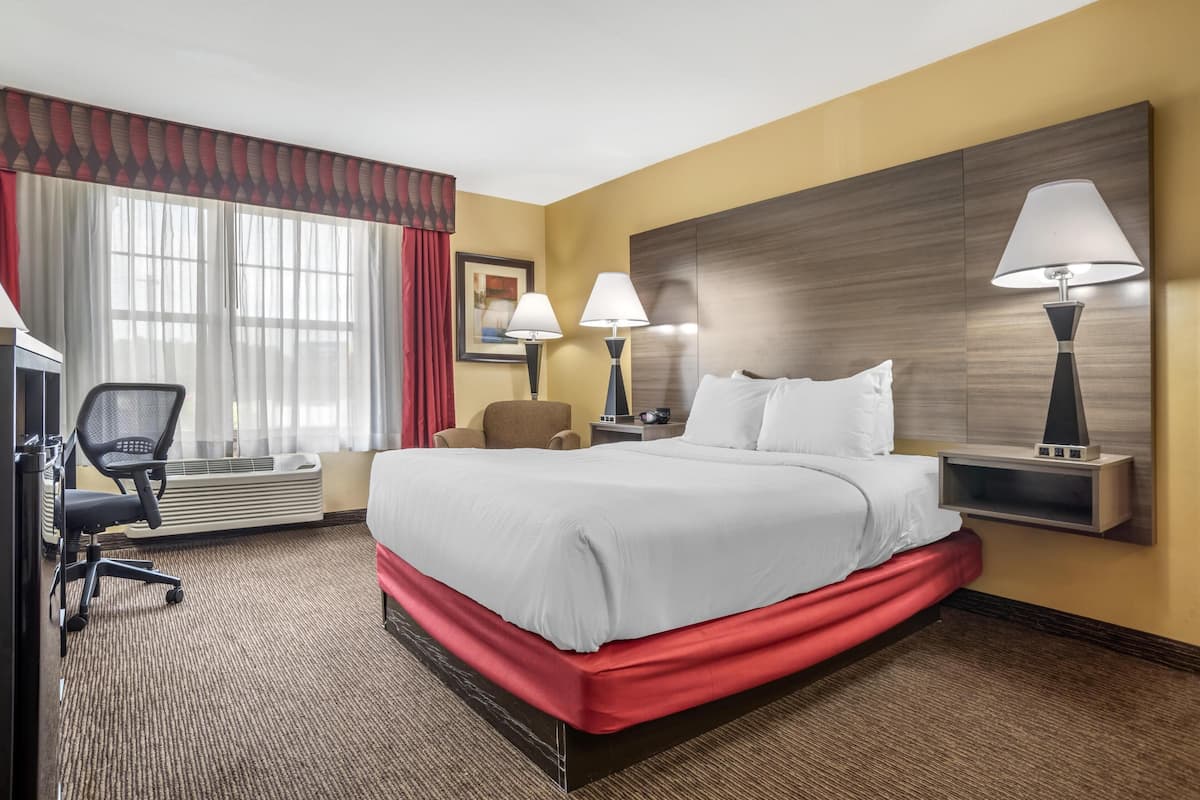 Habitación de hotel con una cama grande, dos lámparas de noche, un escritorio con silla y una ventana con cortinas.