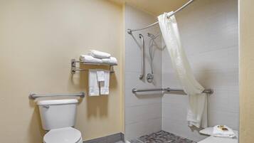 Un baño accesible en silla de ruedas, con inodoro, barras de apoyo, ducha con cortina blanca y una pequeña mesa con toalla.