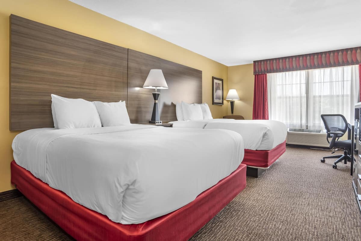Habitación de hotel con dos camas, un escritorio, una silla y una ventana con cortinas.