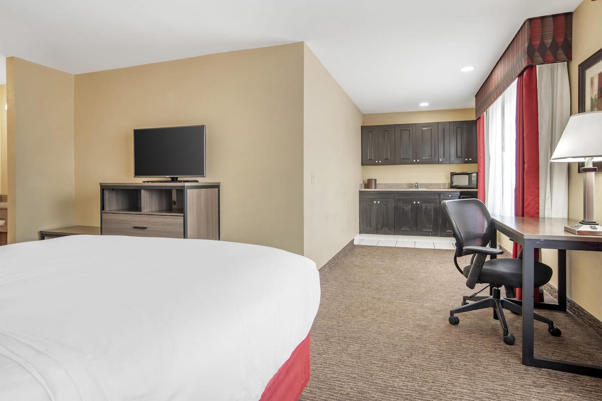 Habitación de hotel con cama, escritorio, silla, televisor, kitchenette y cortinas.