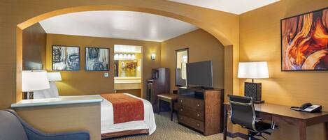 A hotel room with a bed, desk, chair, TV, and artwork on the walls.