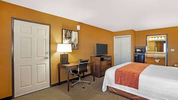 Une chambre d’hôtel équipée d’un lit, d’un bureau, d’une chaise, d’une télévision et d’une salle de bain avec un miroir et un lavabo.