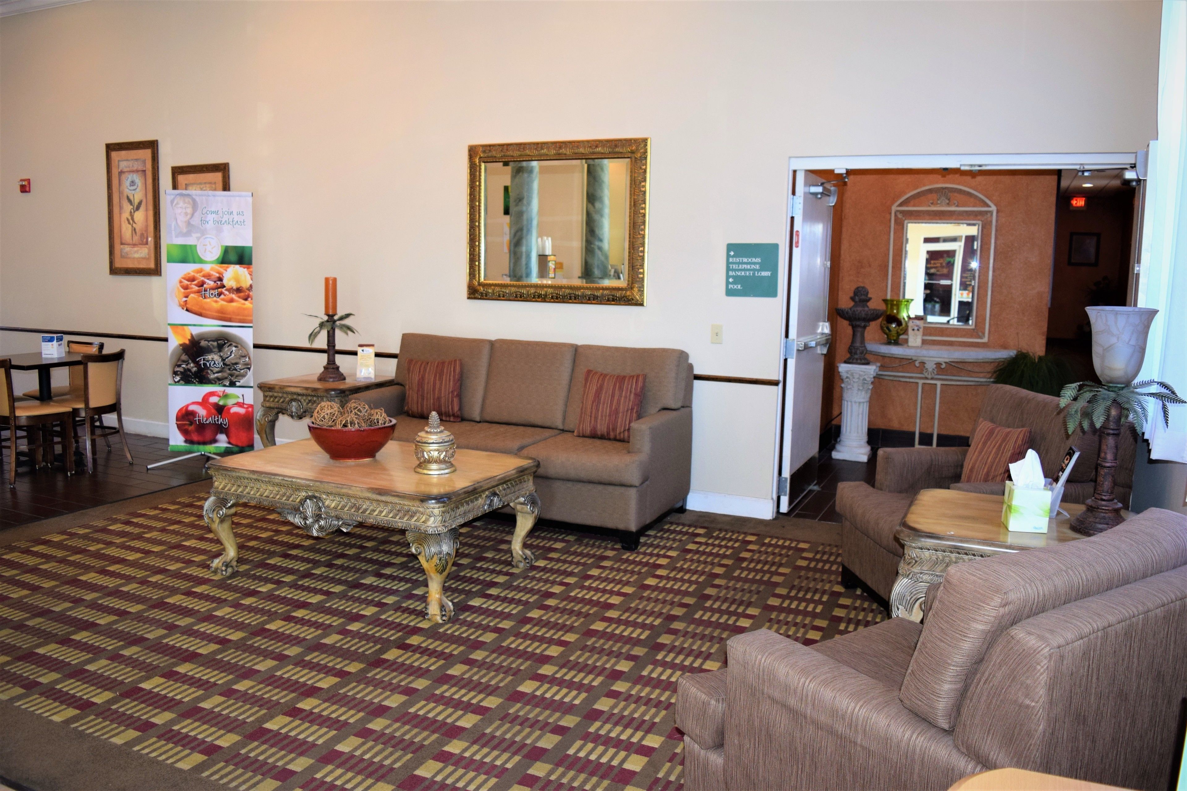 A hotel lobby with a patterned carpet, a sofa, a coffee table, and a mirror on the wall.
