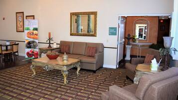 A hotel lobby with a patterned carpet, a sofa, a coffee table, and a mirror on the wall.