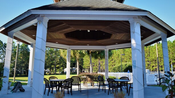 A gazebo with a wooden roof and white columns, surrounded by outdoor tables and chairs, set in a park with trees and a white fence in the background. - Quality Inn Conference Center at Citrus Hills (Hernando)