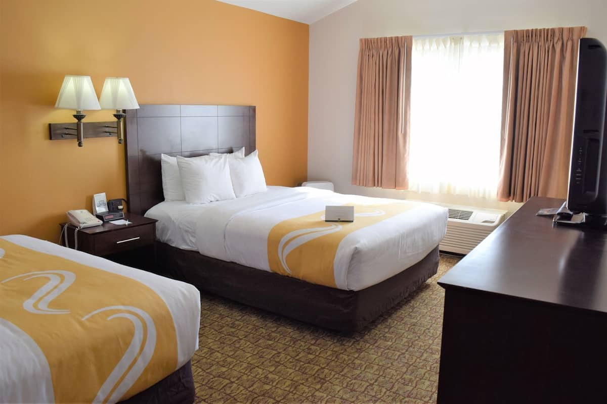A hotel room with two beds, a desk, a phone, and a television.