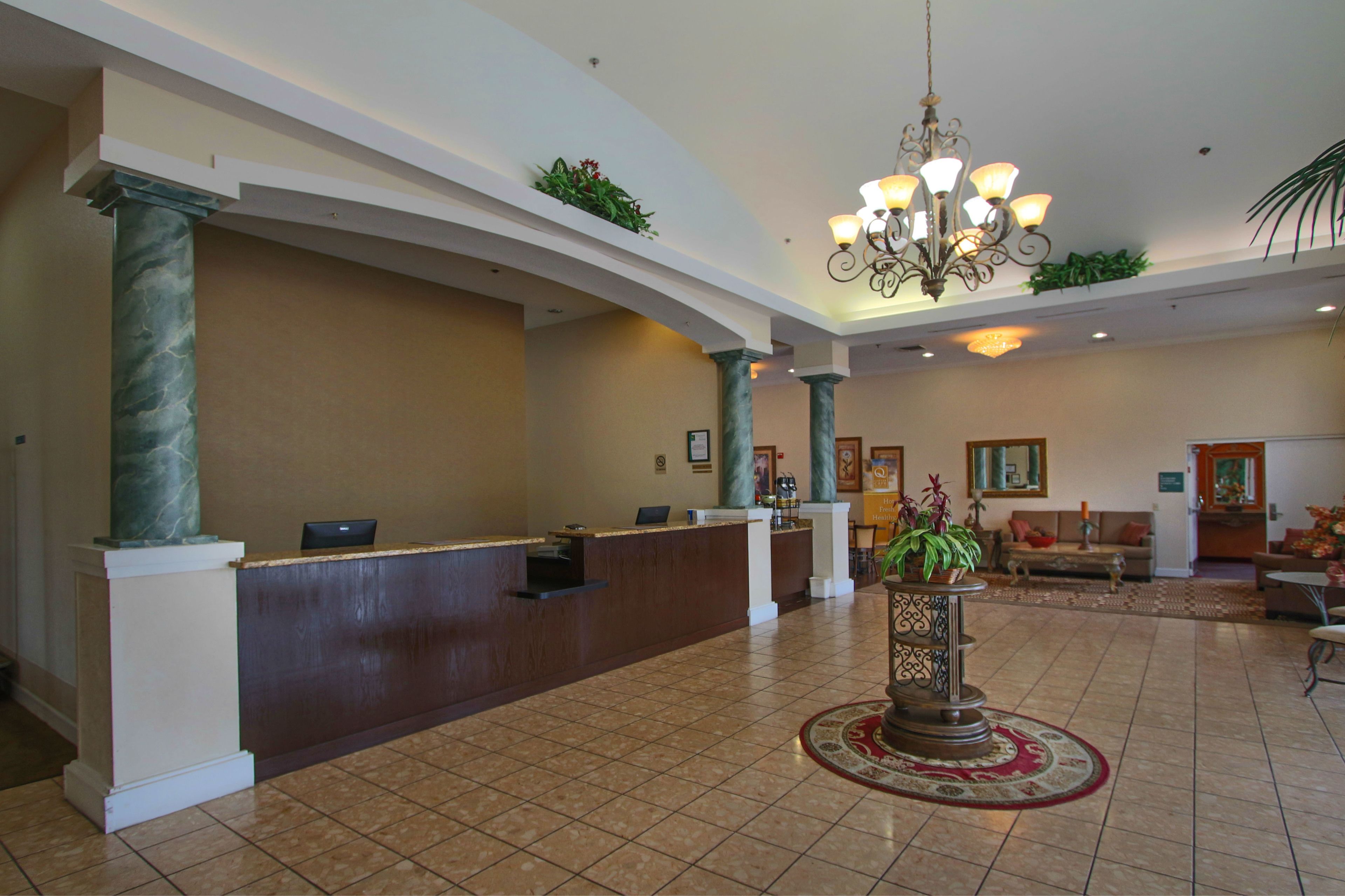 A spacious lobby with a reception desk, marble columns, a chandelier, and a decorative plant.