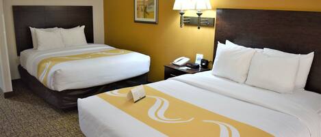 A hotel room with two beds, a nightstand with a lamp, and a wall-mounted telephone.