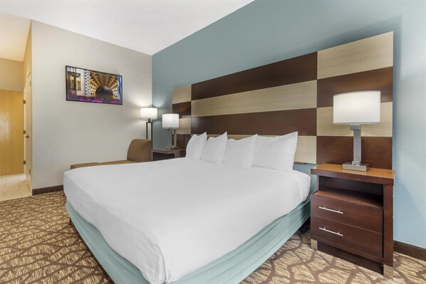 A hotel room with a large bed, two bedside tables with lamps, a wall-mounted artwork, and a patterned carpet.