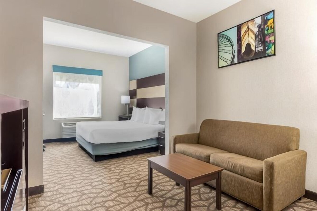 A hotel room with a bed, a sofa, a coffee table, and a painting on the wall.