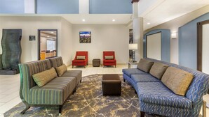A spacious lobby with a high ceiling, two sofas with patterned upholstery, a small ottoman, and a cityscape painting on the wall. - Best Western Joliet Inn & Suites (Joliet)