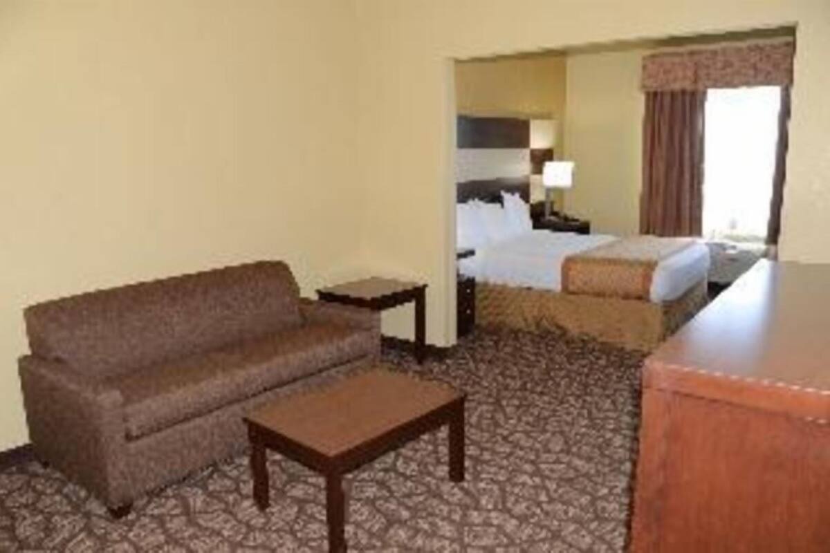 A hotel room with a sofa, a small table, a bed with a headboard, and a window with curtains.