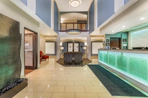 A hotel lobby with a reception desk, seating area, and a glass wall.