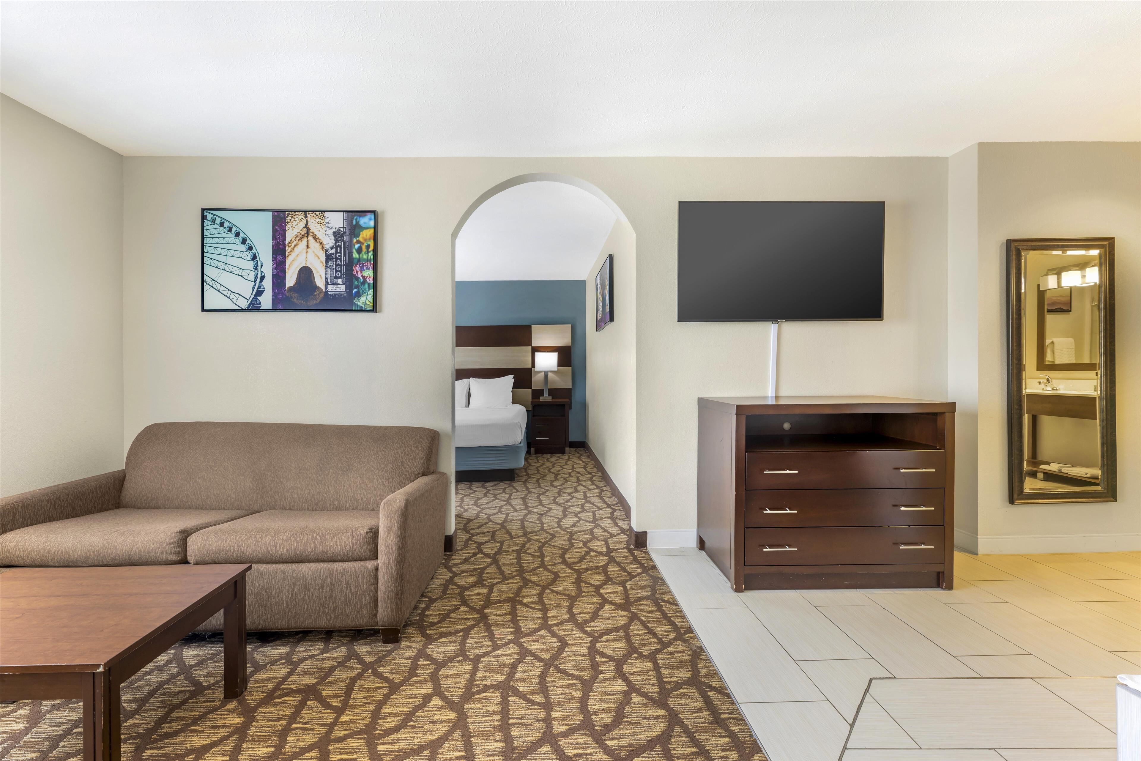 A hotel room with a sofa, a TV, a dresser, and a patterned carpet.