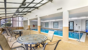 An indoor pool area with a glass ceiling, poolside chairs, and a tiled table. - Best Western Joliet Inn & Suites (Joliet)