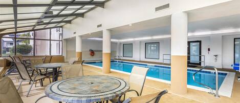 Un espace piscine intérieure doté d’un toit en verre, de sièges au bord du bassin et d’un panneau indiquant qu’il est interdit de plonger.
