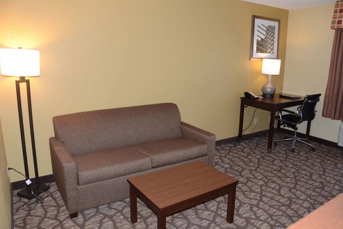 A hotel room with a sofa, a small wooden table, a desk with a chair, and two lamps.
