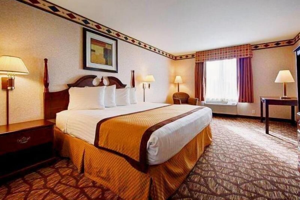 A hotel room with a large bed, two bedside tables, a chair, a window with curtains, and a painting on the wall.