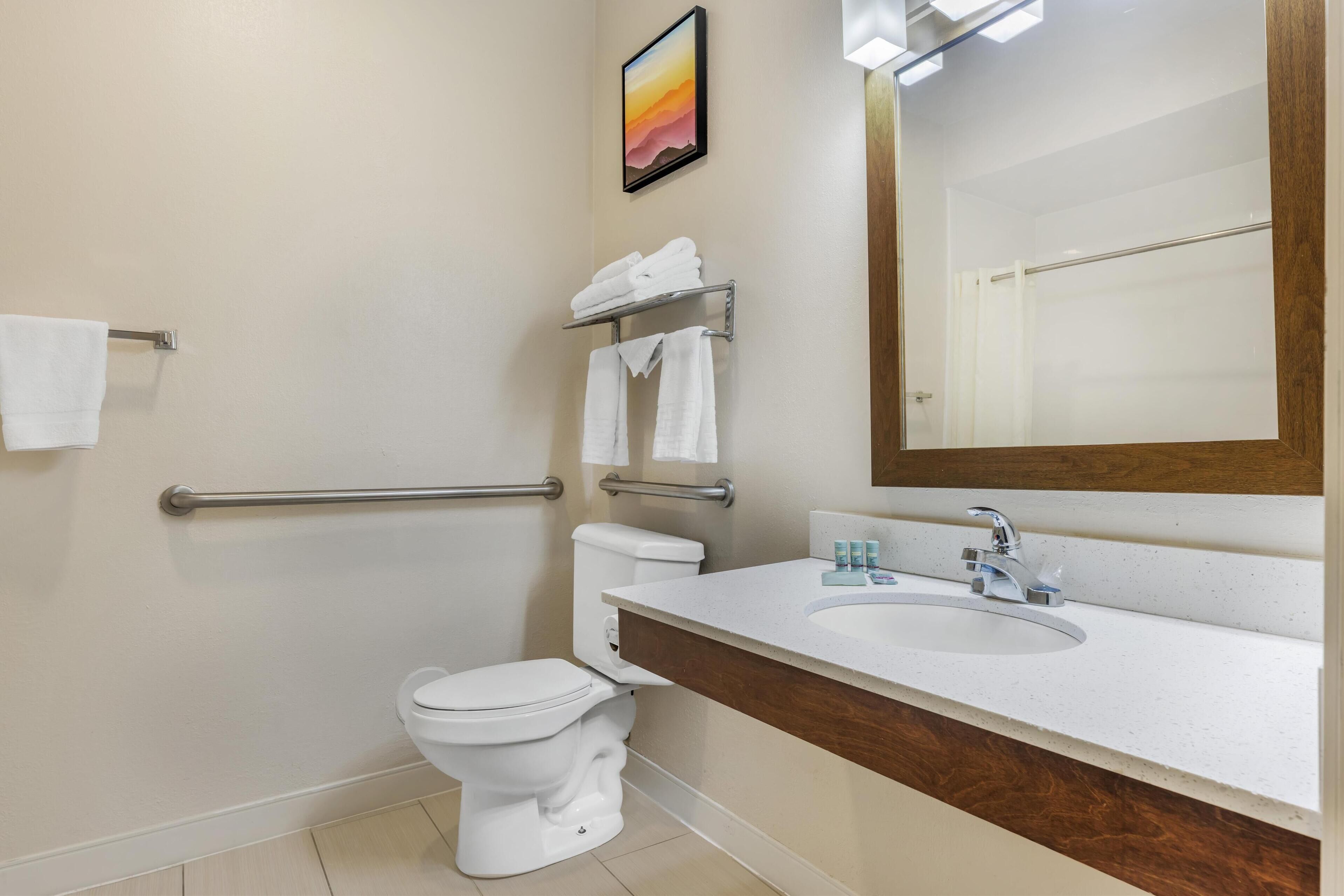 Un baño moderno con inodoro, lavamanos y barras de apoyo.