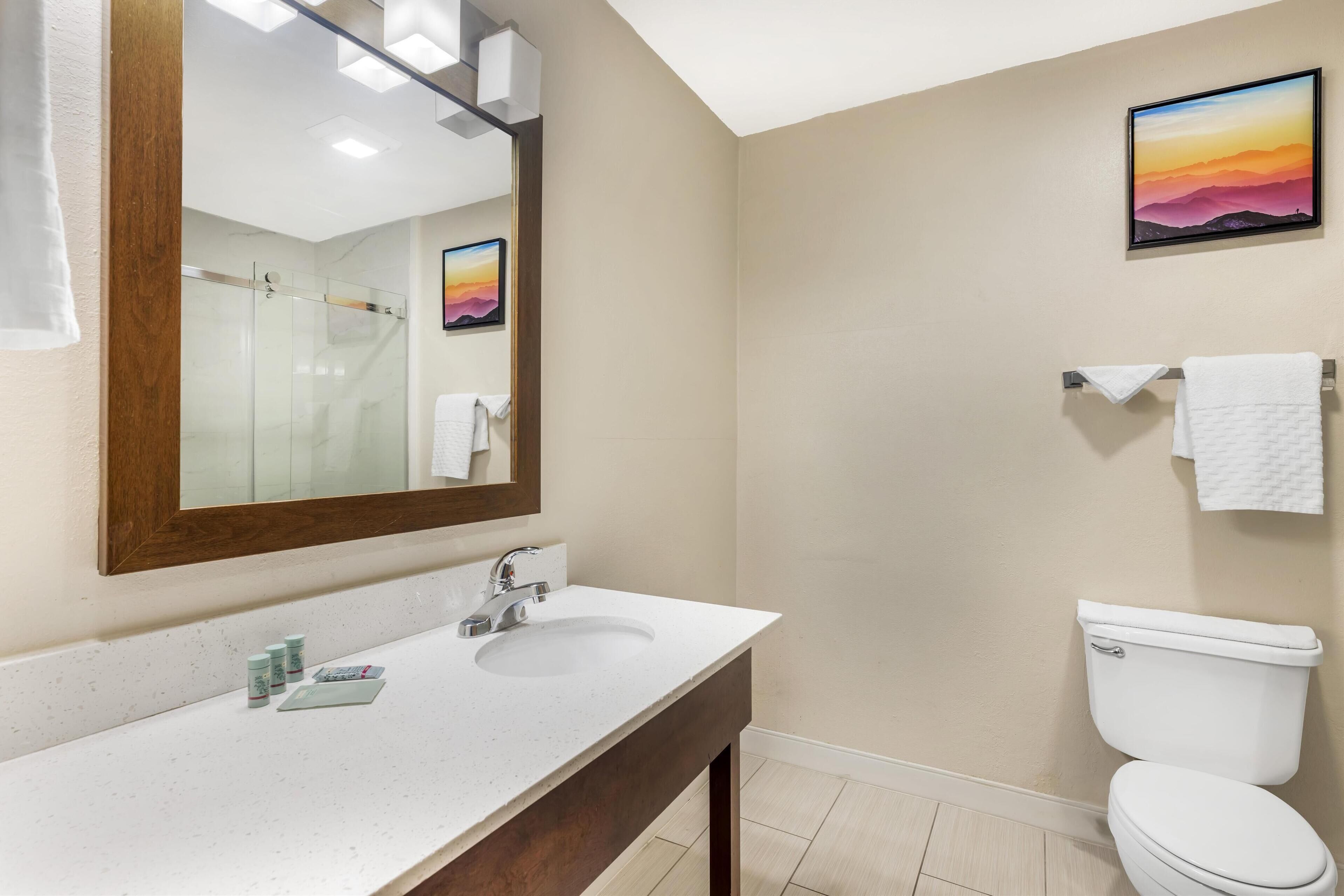 A bathroom with a white sink, mirror, and toilet. There is a towel rack with a white towel and a framed picture on the wall.