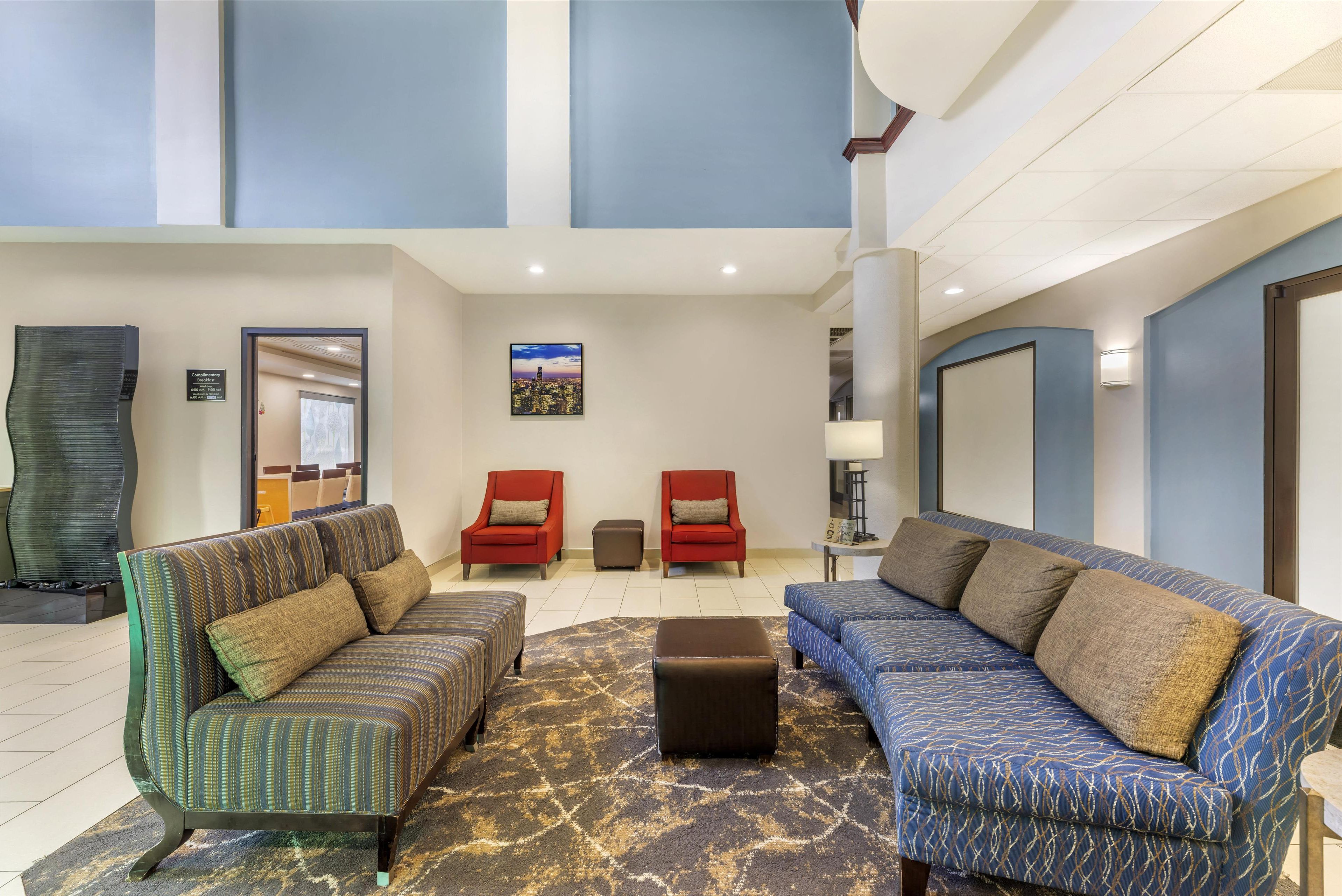 A spacious lobby with a high ceiling, two sofas with patterned upholstery, a small ottoman, and a cityscape painting on the wall.