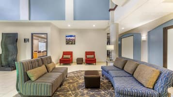 A spacious lobby with a high ceiling, two sofas with patterned upholstery, a small ottoman, and a cityscape painting on the wall.