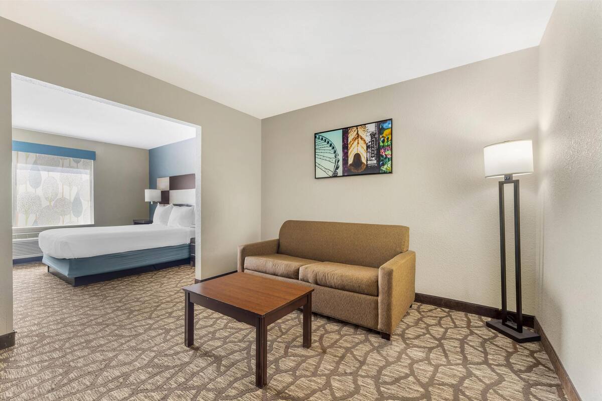 A hotel room with a bed, a sofa, a coffee table, a lamp, and a painting on the wall.